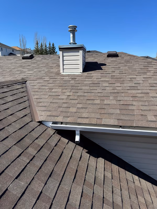 Chimney chase and flue cap on brown shingle roof