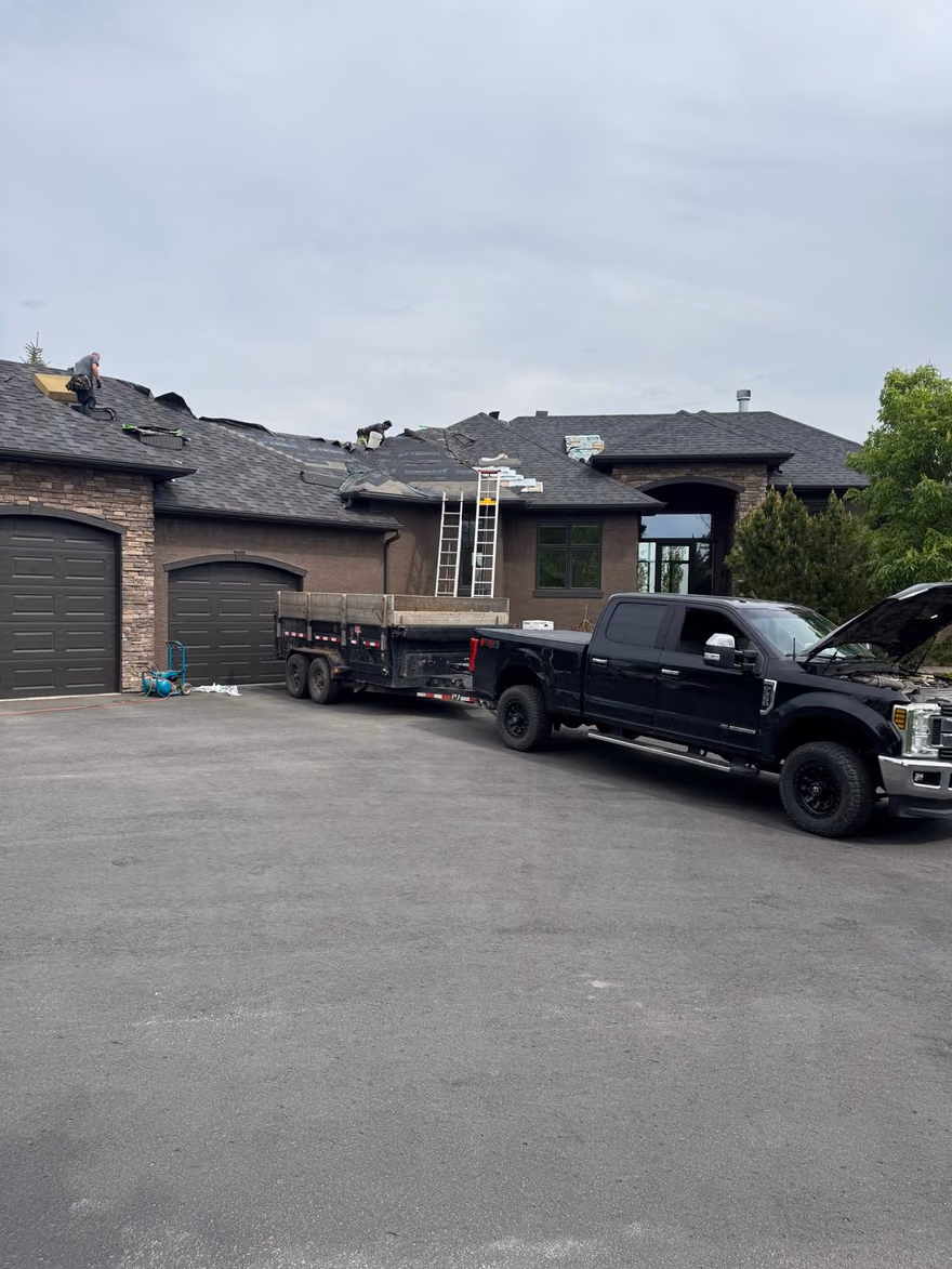 Crew on roof with dump trailer in driveway