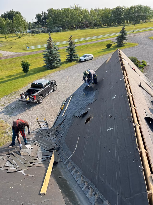 Crew stripping old shingles beside parked pickup truck