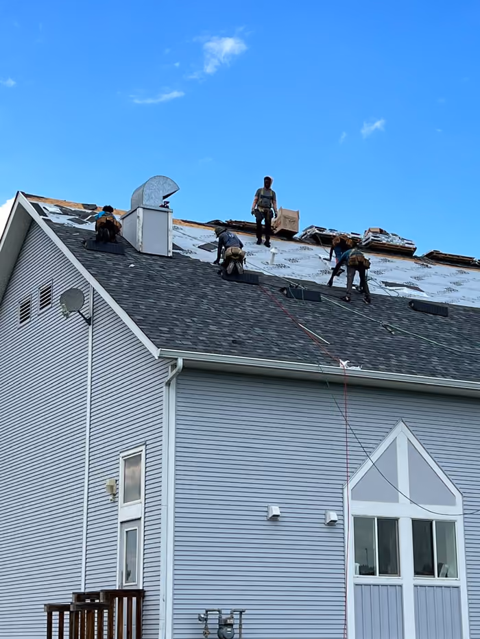 Crew tearing off shingles along ridge ground view