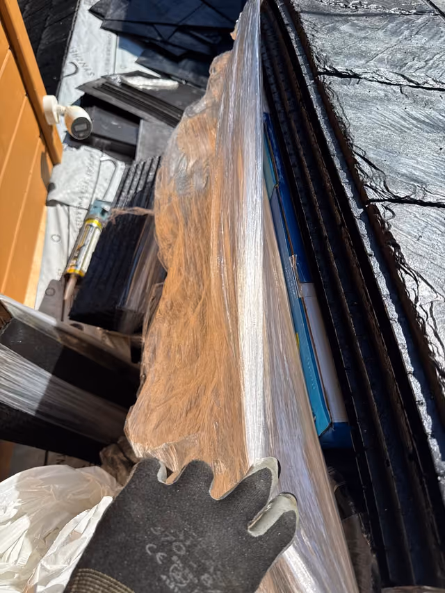 Hand holding synthetic slate shingle at roof edge