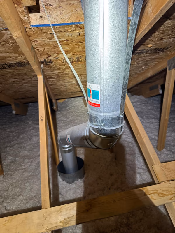 Metal exhaust duct elbow above attic insulation