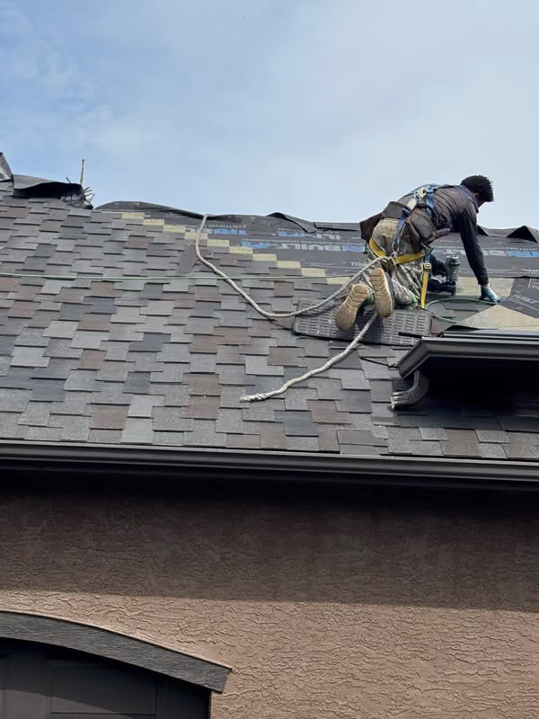 Roofer nailing shingle course with safety harness