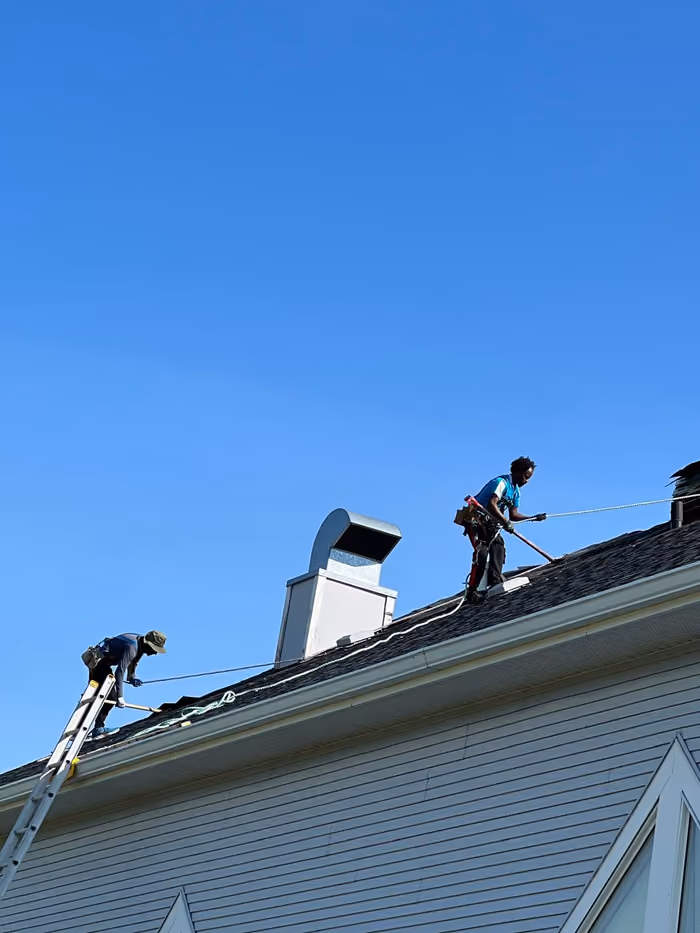 Roofers working along ridge beside chimney chase