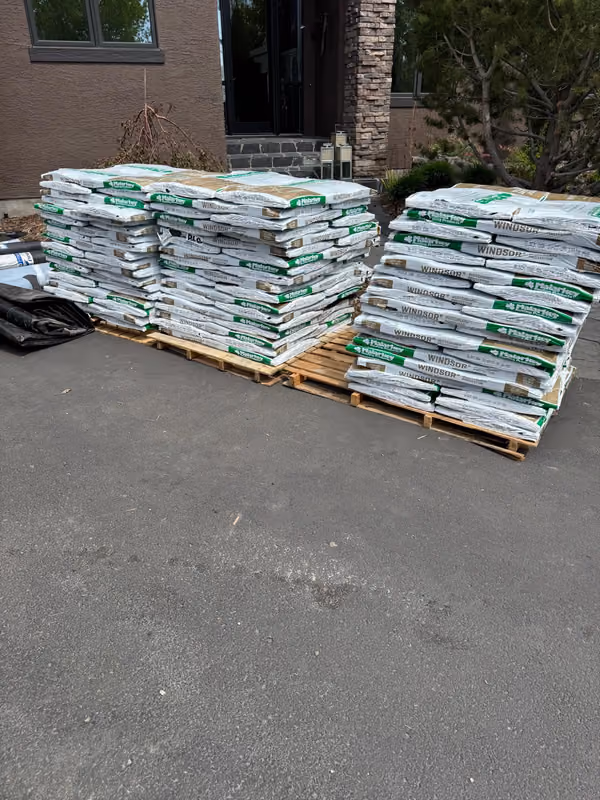 Stacked shingle bundles staged on driveway pallets